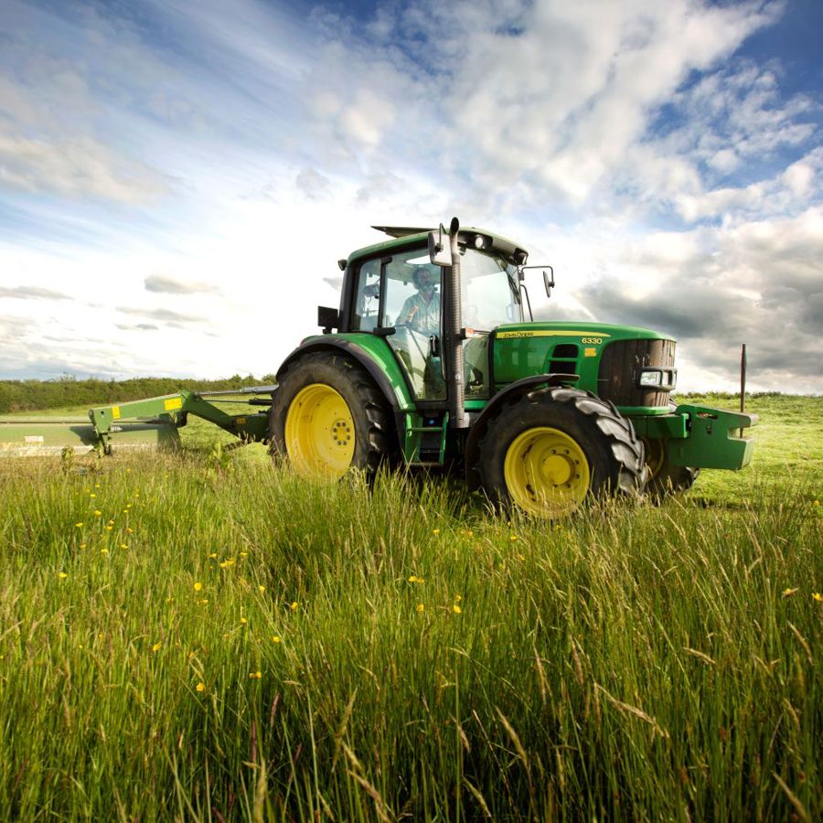A tractor cutting silage in a meadow full of grass and flowers